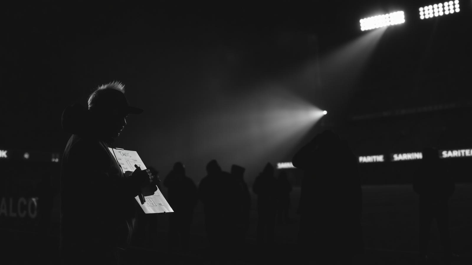 Silhouetted football coach studying tactics on the sideline